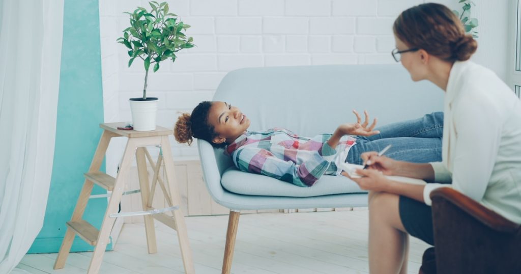 A young girl talks to a therapist on a couch.