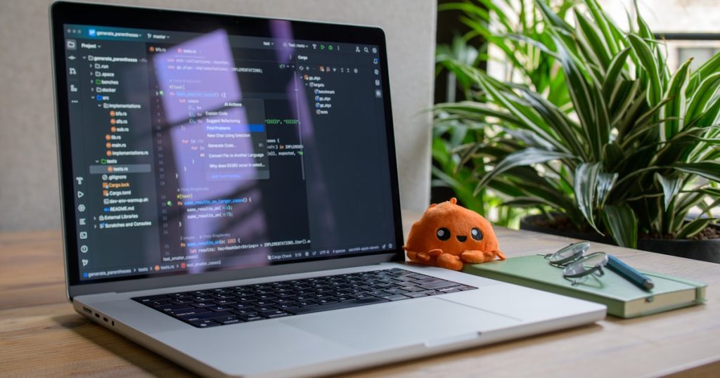 Laptop displaying code with small stuffed toy nearby
